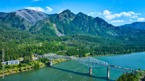 Картината върху платно Aerial View of Steel Bridge Over River in Lush Mountain Valley