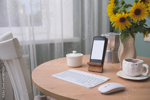  Home workplace in interior - mockup blank white screen, keyboard, computer mouse, cup of coffee, vaze with suflowers on wooden table near the window in living room. photo