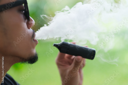Vaping with an electronic cigarette vape device concept. Smoking with an E-cigarette blowing smoke from mouth, close up vaper doing modern alternative to tobacco addictive habit.