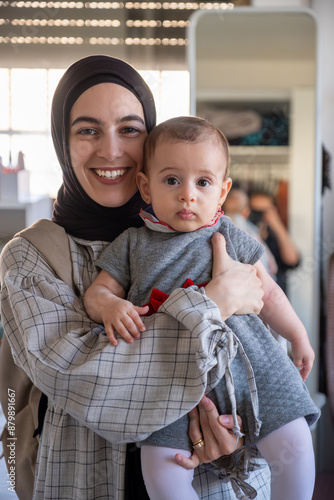 vertical photo for female holding her newborn looking at the camera cheerfully and well dressed with her little guy to have there first celebration and family moments