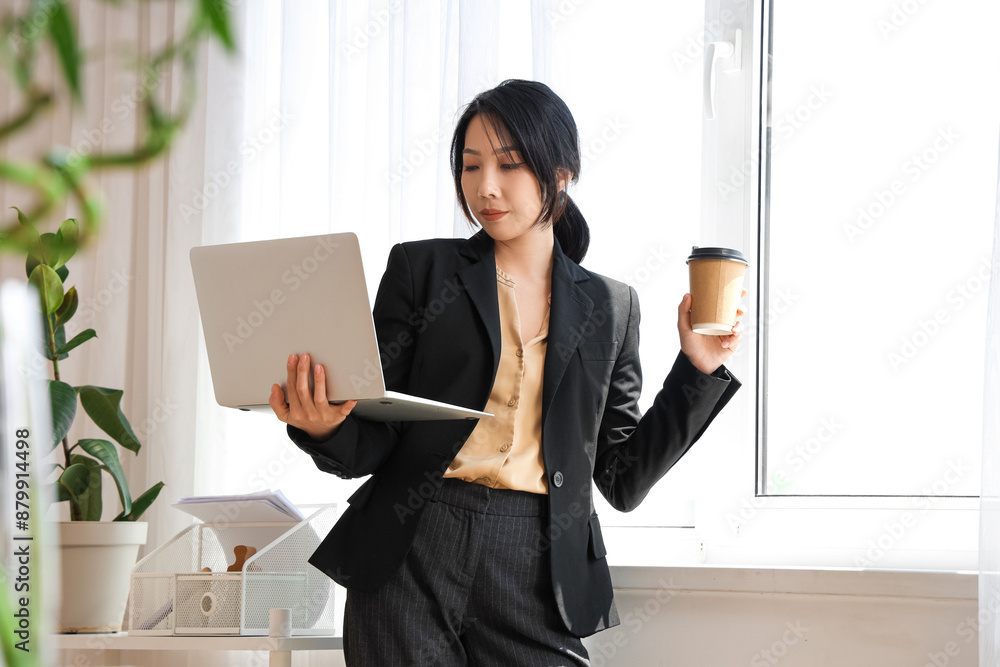 Young Asian businesswoman with laptop and cup of coffee working in office Young Asian businesswoman with laptop and cup of coffee working in office