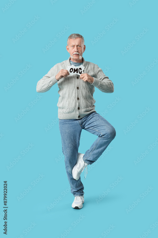 Shocked senior man holding speech bubble with word OMG on blue background Shocked senior man holding speech bubble with word OMG on blue background