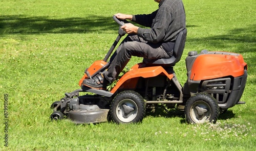 Obraz na plátně A man drives and mows grass in the garden with a lawnmower.