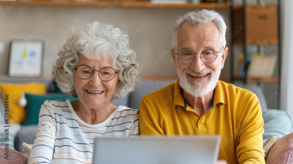 A happy elderly couple with glasses, sitting close together, smiling as they use a laptop in a cozy and well-decorated living room, showcasing love and companionship. A happy elderly couple with glasses, sitting close together, smiling as they use a laptop in a cozy and well-decorated living room, showcasing love and companionship.