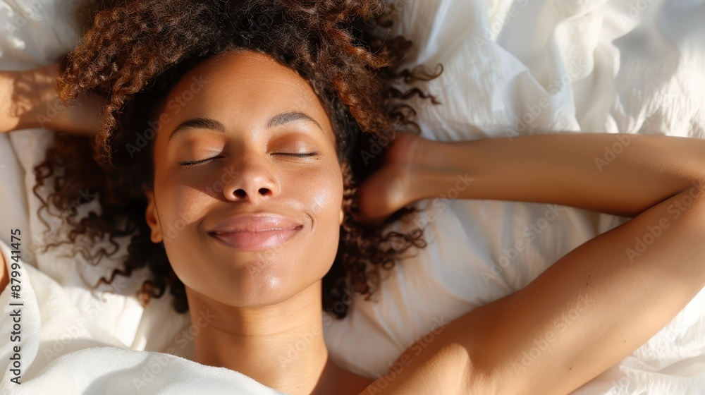 A peaceful woman with curly hair, eyes closed, and arms resting behind her head while lying in a cozy bed; the soft morning light enhances the serene atmosphere. A peaceful woman with curly hair, eyes closed, and arms resting behind her head while lying in a cozy bed; the soft morning light enhances the serene atmosphere.