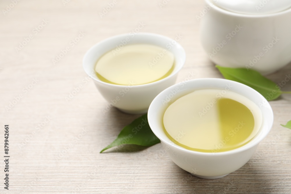Refreshing green tea in cups and leaves on wooden table, closeup Refreshing green tea in cups and leaves on wooden table, closeup