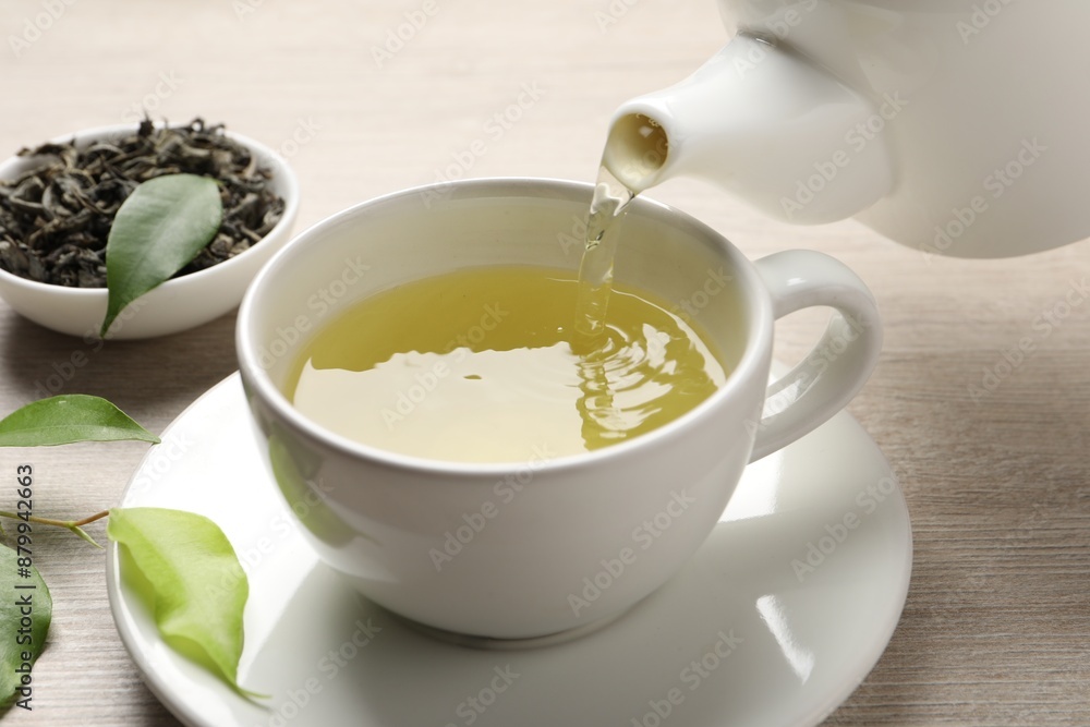 Pouring refreshing green tea into cup at wooden table, closeup Pouring refreshing green tea into cup at wooden table, closeup