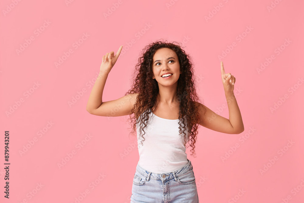 Happy young African-American woman pointing at something on pink background Happy young African-American woman pointing at something on pink background