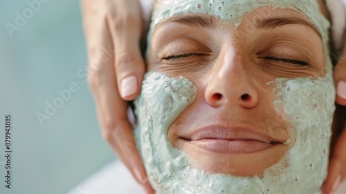 A close-up of a woman receiving a facial massage while wearing a green face mask, eyes closed, depicting ultimate relaxation and self-pampering in a spa environment. photo