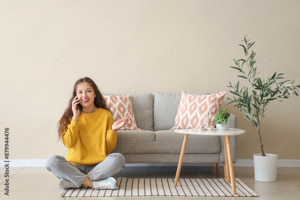 Young Asian woman talking by mobile phone on carpet near sofa at home Young Asian woman talking by mobile phone on carpet near sofa at home