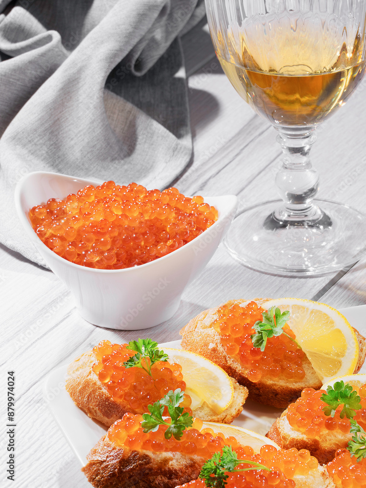 Salmon caviar in a white bowl and sandwiches with red caviar with white wine. Gourmet food up close. Seafood and delicatessen.