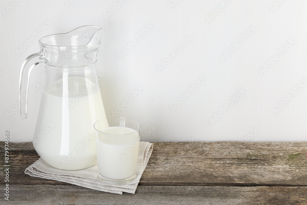 Jug and glass of fresh milk on wooden table, space for text Jug and glass of fresh milk on wooden table, space for text