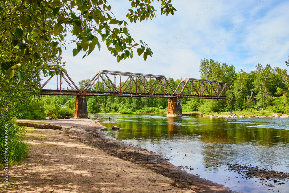 Fototapeta premium Rusty Truss Bridge over Calm River with Reflection Eye Level Perspective