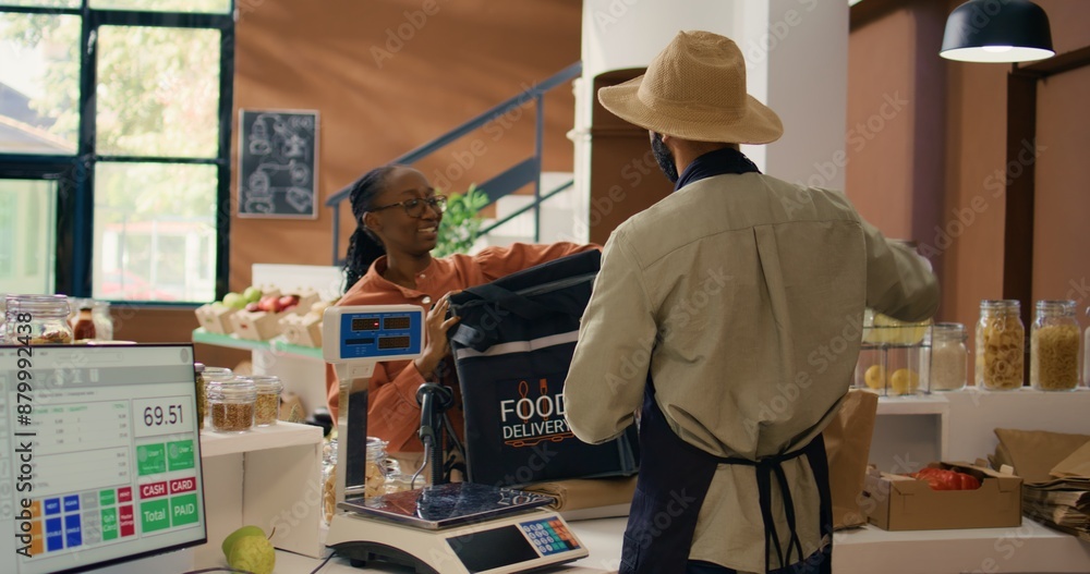 Vendor gives food order for delivery, putting homegrown organic veggies in backpack. African american woman courier coming to get bio supermarket merchandise for local customers. Vendor gives food order for delivery, putting homegrown organic veggies in backpack. African american woman courier coming to get bio supermarket merchandise for local customers.