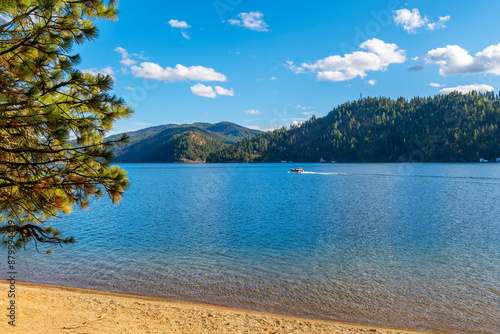 Tableau sur toile A boat passes in front of a small sandy beach at Beacon Point, a stop on the Centennial Trail, on lake Coeur d'Alene's Wolf Lodge Bay, in Coeur d'Alene, Idaho, USA