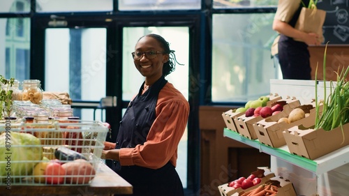 African american woman in local supermarket refilling shelves with freshly harvested produce, small business owner in neighbourhood. Storekeeper arranging pantry products in reusable containers.