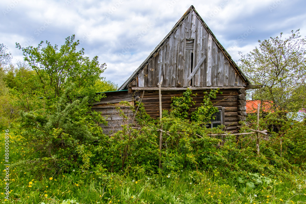 The facade of an abandoned wooden house with windows. The old residential architecture is destroyed and abandoned. A log wall with windows and a roof. The facade of an abandoned wooden house with windows. The old residential architecture is destroyed and abandoned. A log wall with windows and a roof.
