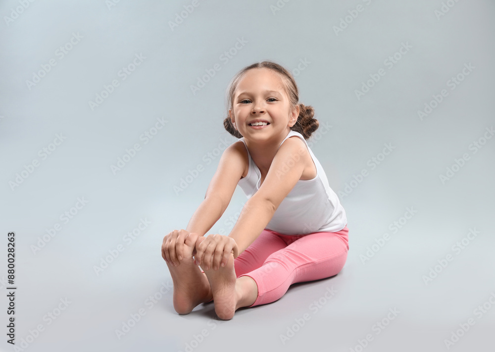 Cute little girl stretching on grey background