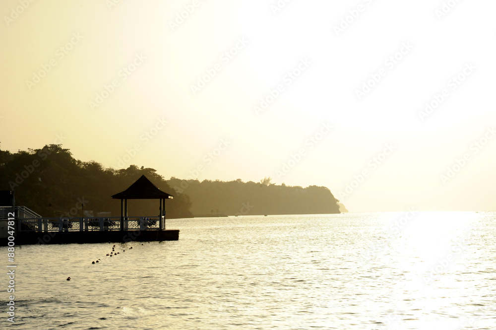 Silhouetted gazebo by the sea during sunset with a distant shoreline Silhouetted gazebo by the sea during sunset with a distant shoreline
