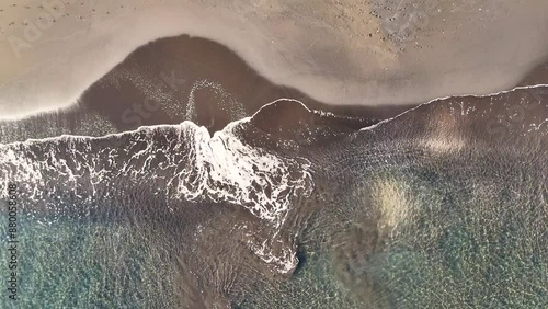 Ocean waves crash onto the black sand beach on the tropical island Tahiti in French Polynesia. Drone aerial footage looking down perspective. 