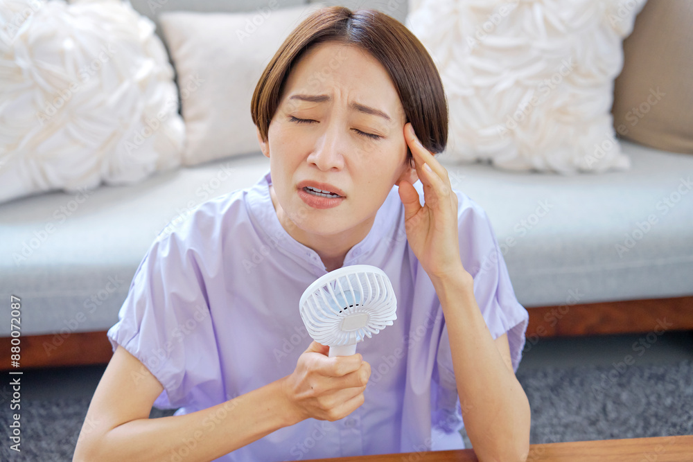 蒸し暑いリビングで携帯扇風機を使う女性