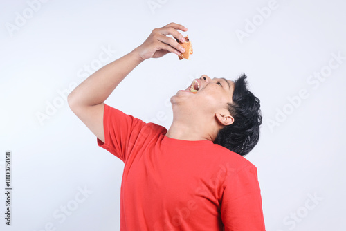 Excited Young Asian Man Devouring Delicious Burger Isolated on White Background.