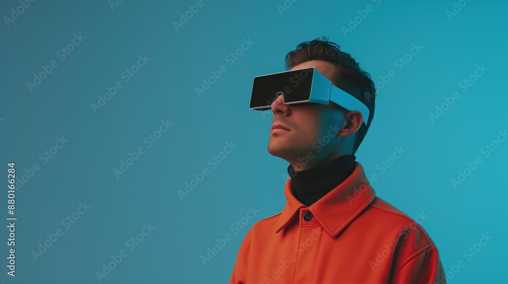 Futuristic vision, man in orange coat wearing large VR headset against blue background, exploring immersive technology, modern digital experience, forward-looking innovation. Futuristic vision, man in orange coat wearing large VR headset against blue background, exploring immersive technology, modern digital experience, forward-looking innovation.