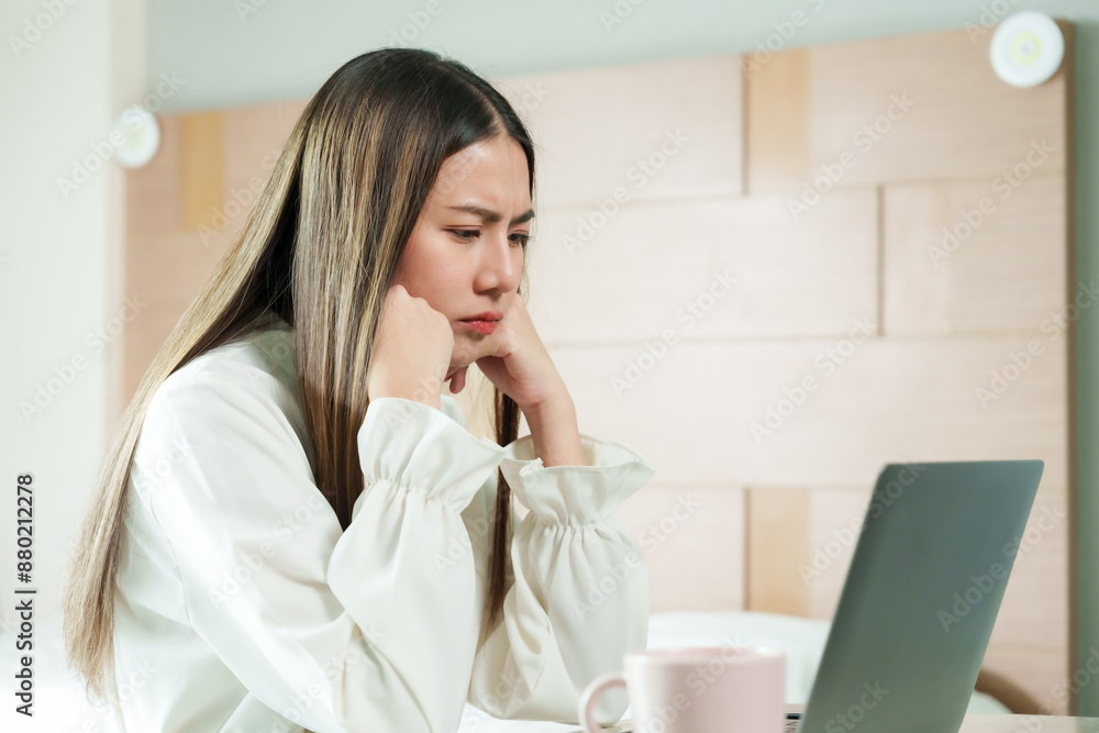 Beautiful Asian woman focused on laptop while working from home on bed, pink cup on table. Cozy bedroom setting, modern lifestyle, challenges of remote work, maintaining work-life balance. Beautiful Asian woman focused on laptop while working from home on bed, pink cup on table. Cozy bedroom setting, modern lifestyle, challenges of remote work, maintaining work-life balance.
