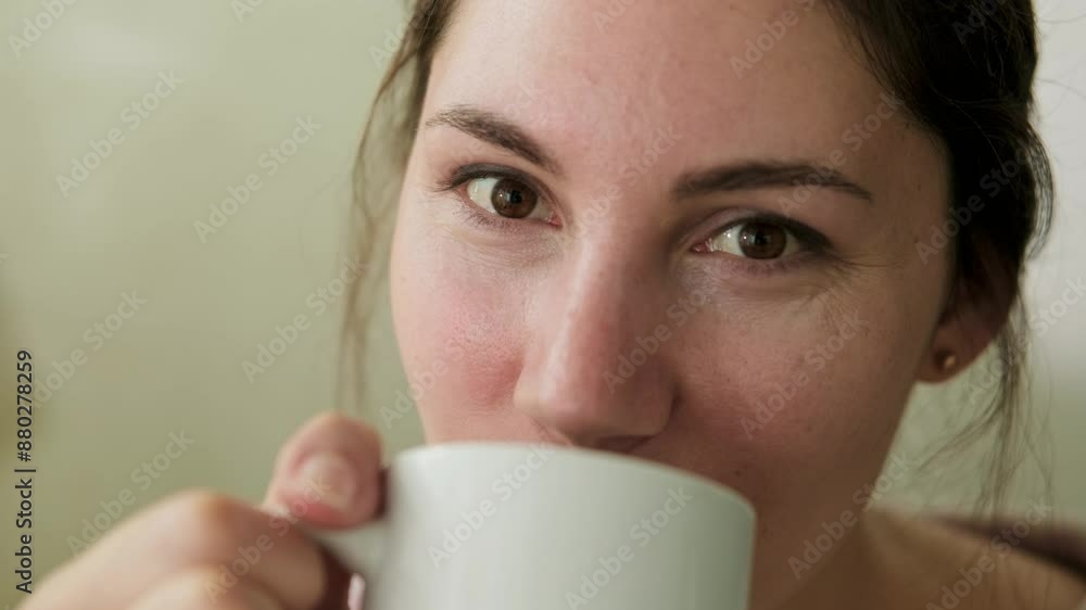 Close-up of an attractive woman holding a cup with her hands, taking a sip of coffee on a sunny morning, smiling and looking at the camera Close-up of an attractive woman holding a cup with her hands, taking a sip of coffee on a sunny morning, smiling and looking at the camera