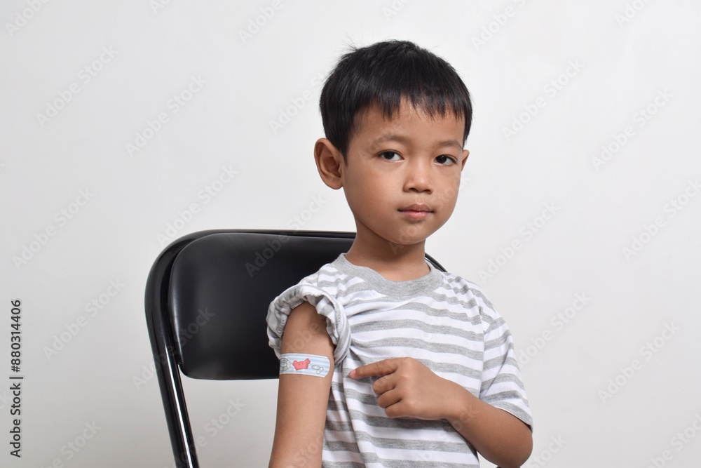 Asian boy shows his arm with bandage after virus vaccine. Child vaccination. Protect your child with vaccine concept. copy space