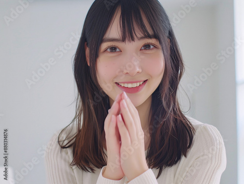 ナチュラルな笑顔で手を合わせるポーズの若いアジア人女性