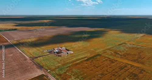 Flying closer to the little location in the dessert for drilling the natural resources. Clouds throw shadows on the immense field on sunny day.