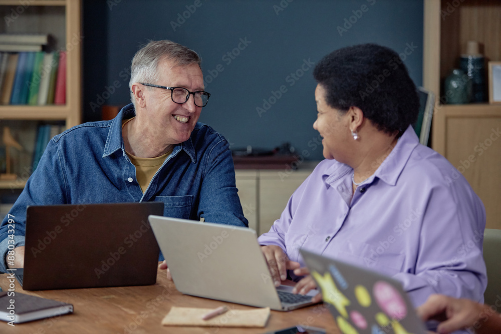 Portrait of smiling senior man talking to woman while using laptop together in computer class for adults Portrait of smiling senior man talking to woman while using laptop together in computer class for adults