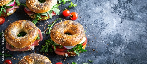 Assorted homemade bagel sandwiches adorned with sesame and poppy seeds cream cheese ham radish arugula cherry tomatoes and cucumbers on a dark concrete backdrop with room for text or images photo