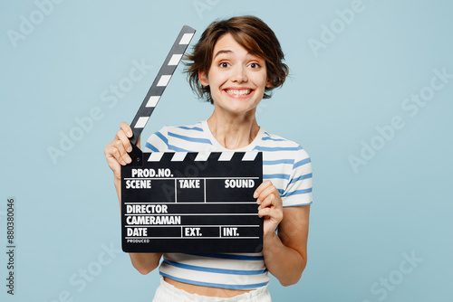 Young cheerful fun woman wear striped t-shirt casual clothes hold in hand classic black film making clapperboard isolated on plain pastel light blue cyan background studio portrait. Lifestyle concept