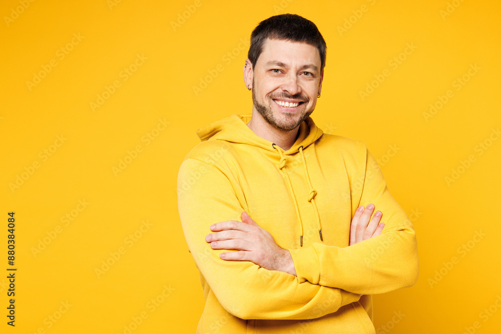 Young smiling happy cheerful confident Caucasian man he wears hoody casual clothes hold hands crossed folded look camera isolated on plain yellow orange background studio portrait. Lifestyle concept. Young smiling happy cheerful confident Caucasian man he wears hoody casual clothes hold hands crossed folded look camera isolated on plain yellow orange background studio portrait. Lifestyle concept.
