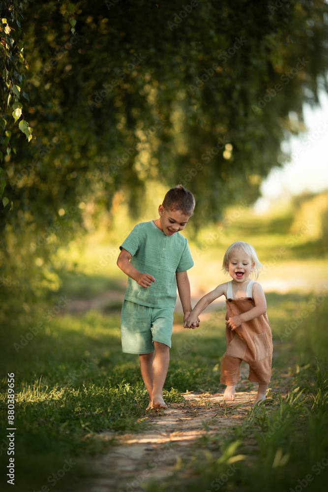 Fototapeta premium two small brothers run together at green nature field on sunset time
