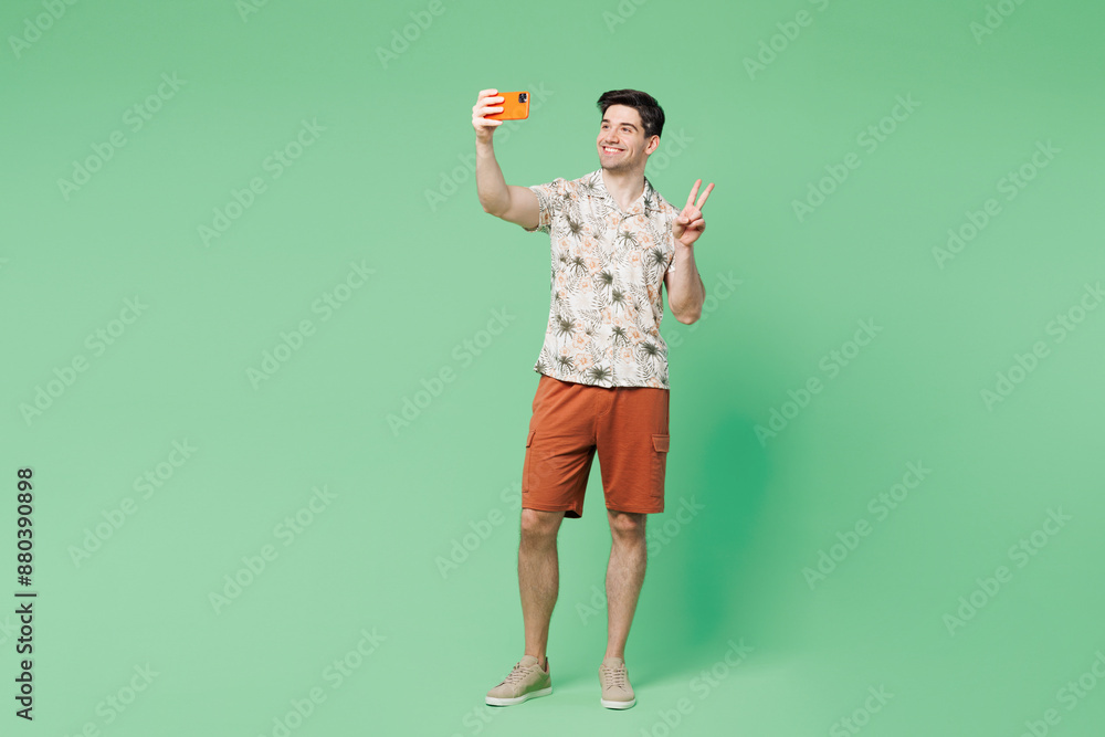 Full body young fun Caucasian man he wear white shirt casual clothes hold in hand use mobile cell phone show v-sign isolated on plain pastel light green background studio portrait. Lifestyle concept. Full body young fun Caucasian man he wear white shirt casual clothes hold in hand use mobile cell phone show v-sign isolated on plain pastel light green background studio portrait. Lifestyle concept.