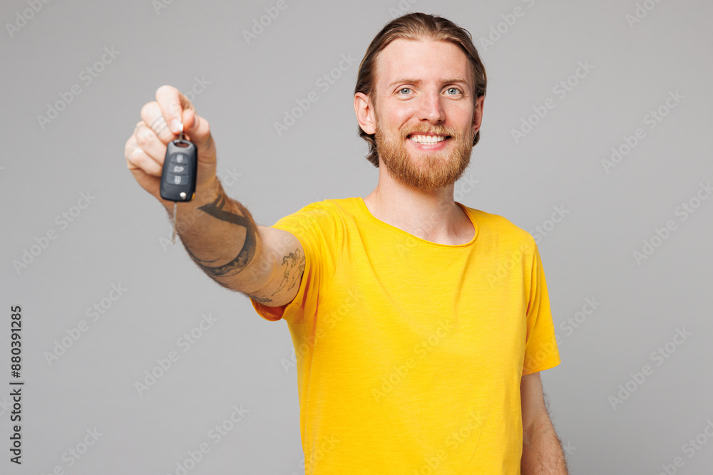 Young smiling happy man he wear yellow t-shirt casual clothes hold in hand car key fob keyless system give stretch hand to camera isolated on plain grey background studio portrait. Lifestyle concept. Young smiling happy man he wear yellow t-shirt casual clothes hold in hand car key fob keyless system give stretch hand to camera isolated on plain grey background studio portrait. Lifestyle concept.