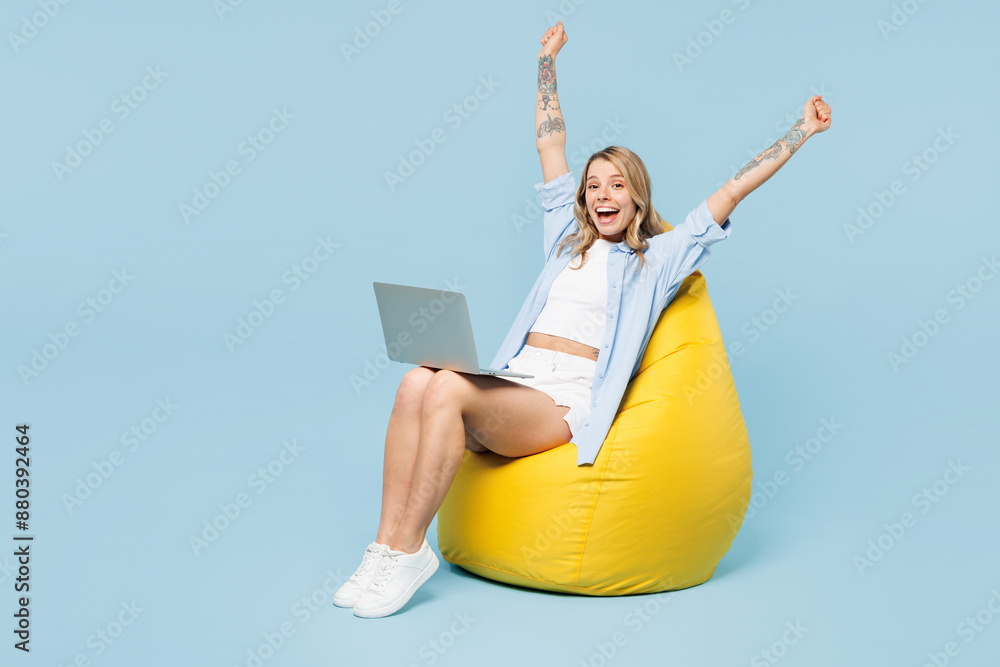 Full body young happy woman wears white top shirt casual clothes sit in bag chair hold use work on laptop pc computer do winner gesture isolated on plain light blue cyan background. Lifestyle concept. Full body young happy woman wears white top shirt casual clothes sit in bag chair hold use work on laptop pc computer do winner gesture isolated on plain light blue cyan background. Lifestyle concept.
