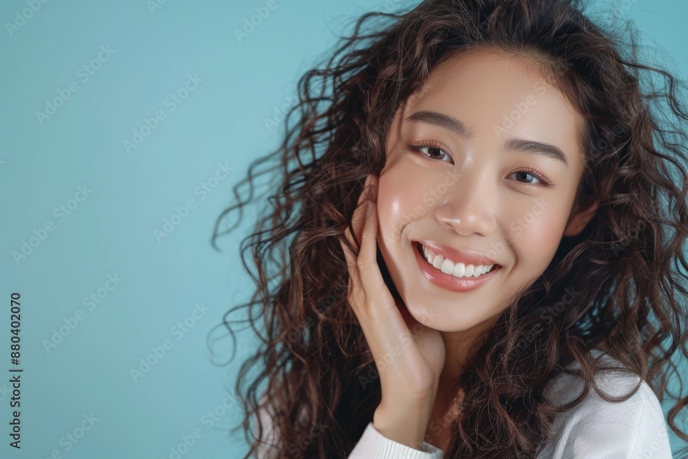 Beautiful Asian beauty with long curly hair, Korean makeup, radiant complexion, healthy facial skin, portrait smile, looking at the mirror on an isolated blue background. Beautiful Asian beauty with long curly hair, Korean makeup, radiant complexion, healthy facial skin, portrait smile, looking at the mirror on an isolated blue background.