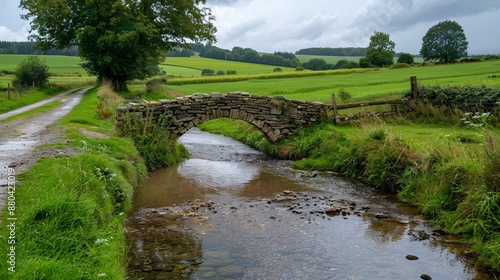 22. A peaceful countryside road with a stone bridge crossing a gentle stream, fields and meadows stretching out beyond