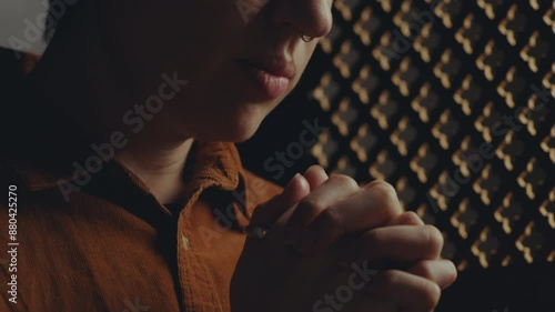 Young woman holding palms together and saying contrition prayer with eyes closed during confession in church. Close-up view