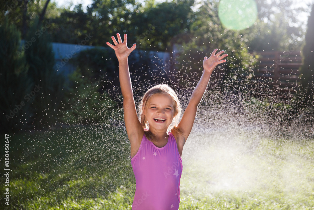 Happy child girl playing with garden hose and having fun with spray of water in sunny backyard. Summer time. Kid girl helps water garden with hose. Enjoying the little things. Summer holiday Happy child girl playing with garden hose and having fun with spray of water in sunny backyard. Summer time. Kid girl helps water garden with hose. Enjoying the little things. Summer holiday