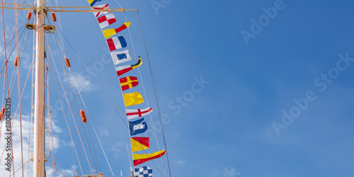 International maritime signal flags on a flagpole and masts on a sailing ship with a blue sky in the background