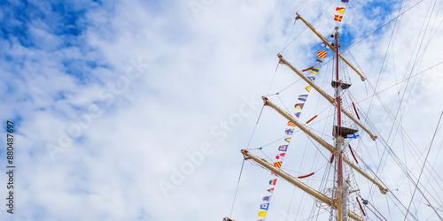Sailing ship mast with flying nautical flags festival celebration decoration in a blue sunny sky and clouds, rigging of old tall ship with colorful bunting strung