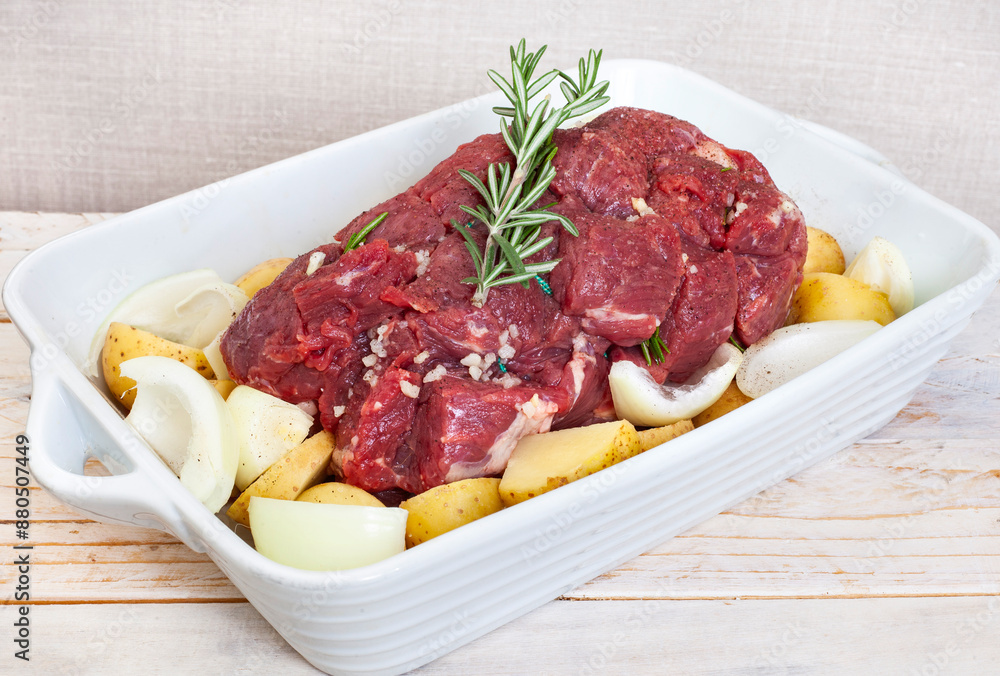 Raw all beef roast prepared with potatoes, onions and garlic in a white square dish ready for the oven Raw all beef roast prepared with potatoes, onions and garlic in a white square dish ready for the oven