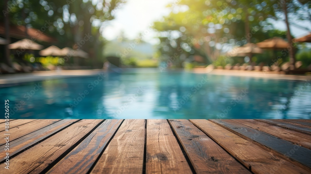 The background of a swimming pool is blurred with an empty wooden table in front of it The background of a swimming pool is blurred with an empty wooden table in front of it