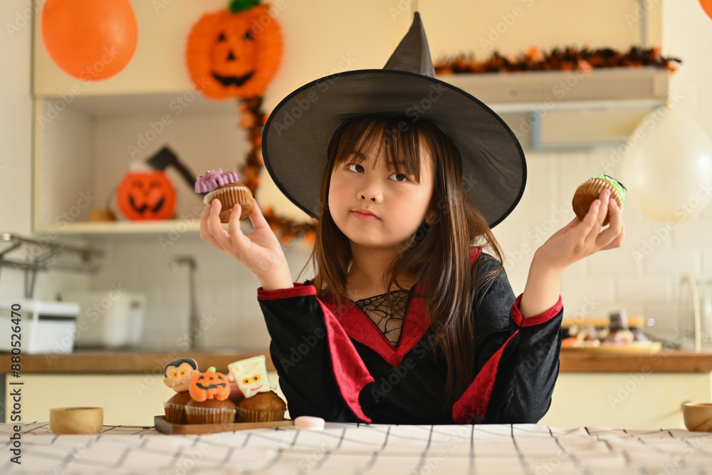 Portrait of cute little girl in witch costumes holding Halloween desserts standing in decorated room Portrait of cute little girl in witch costumes holding Halloween desserts standing in decorated room