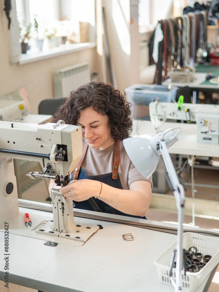 A woman tanner sews a leather belt on a sewing machine. Vertical photo. A woman tanner sews a leather belt on a sewing machine. Vertical photo.